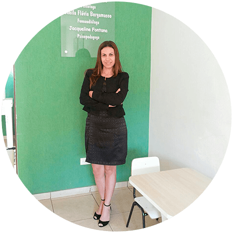 Izabel Morais em seu ambiente profissional Psicóloga Izabel Morais em pé, de braços cruzados, diante de uma parede verde